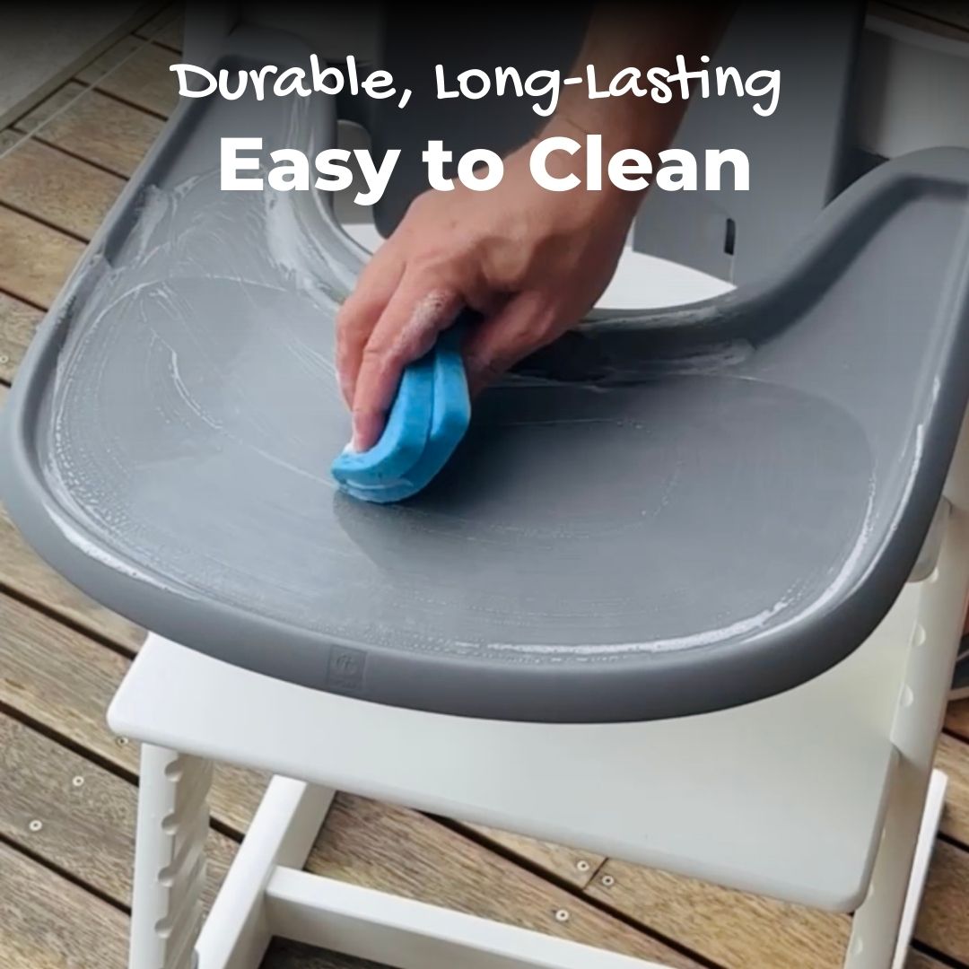 A person cleans a Tripp Trapp high chair tray with a sponge and soap. The tray has installed a suction sticker, which is durable, long-lasting and easy to clean.