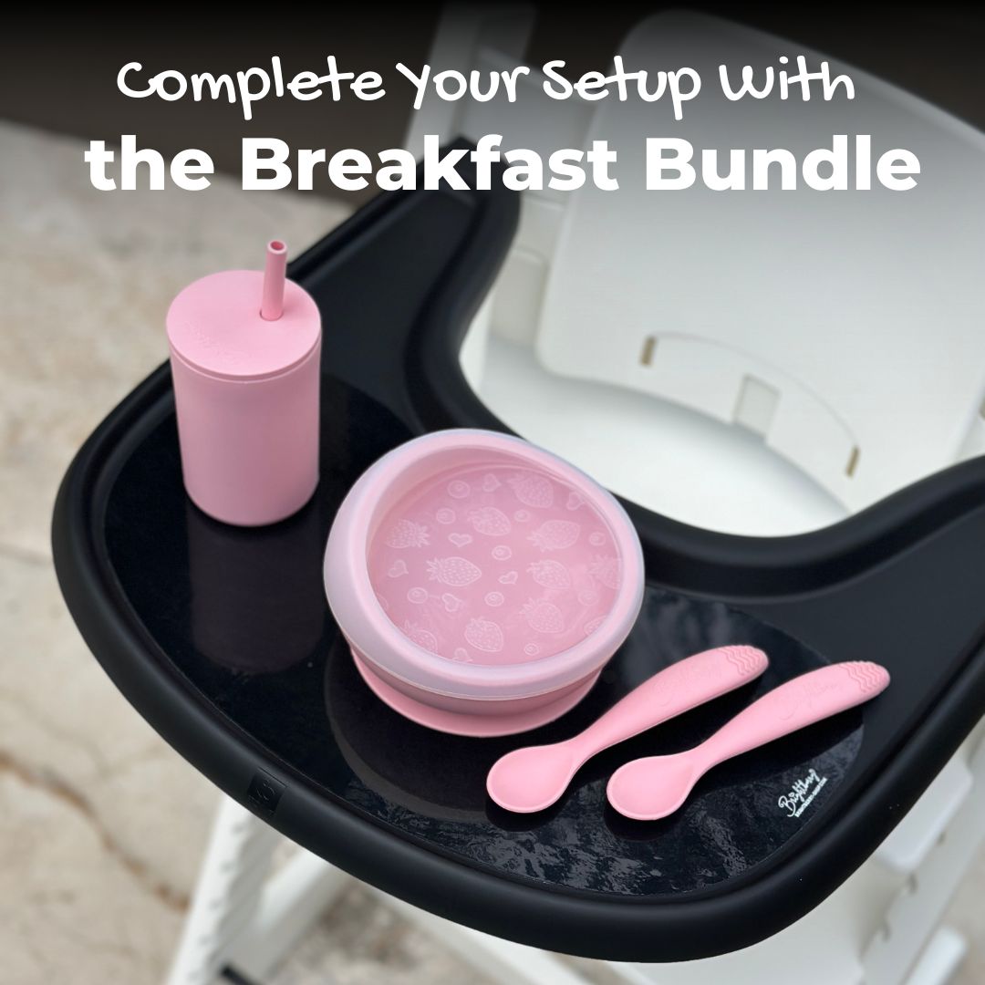 Image is showing white Stokke tripp trapp high chair with a black tray featuring coral ping Brightberry feeding set - the breakfast bundle including a suction bowl with lid,  smoothie cup and self feeding spoons