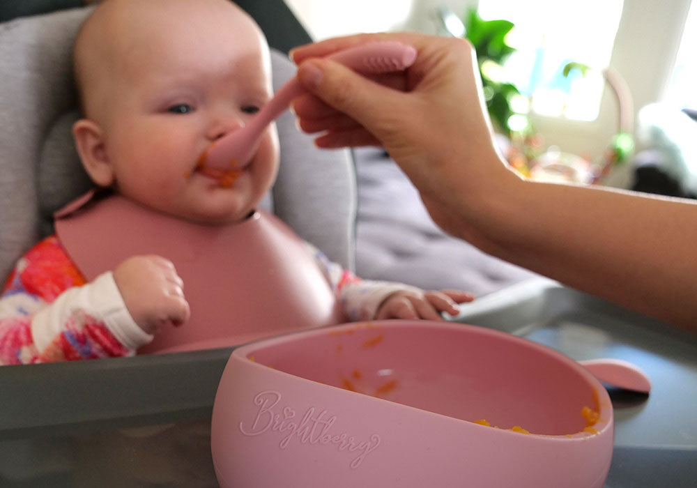 baby starting solids by being spoon fed with food mama prepared in silicone suction bowl and silicone spoon